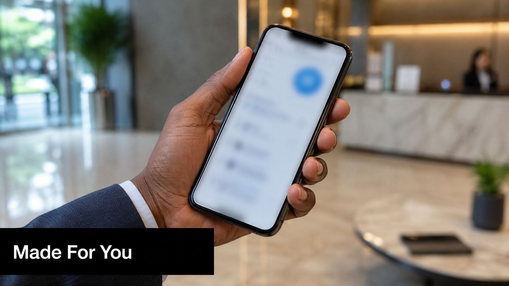 A professional hand holding a smartphone in a bright, modern office lobby setting.
